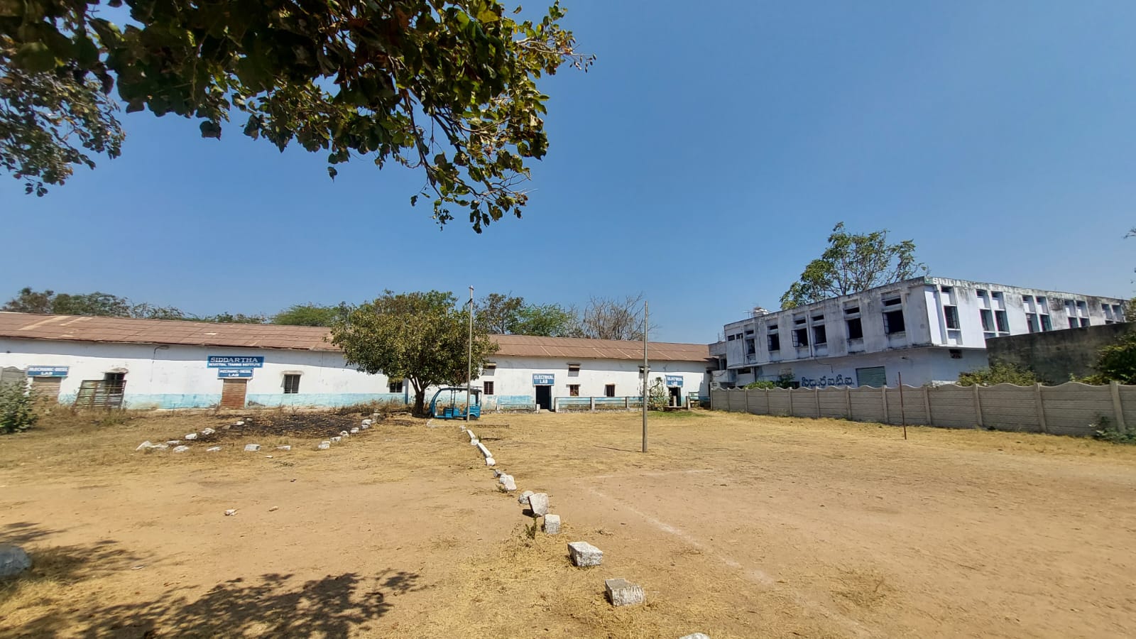 Wide outdoor view of Siddartha ITI campus courtyard with workshop building, classroom block, and labs under a clear sky